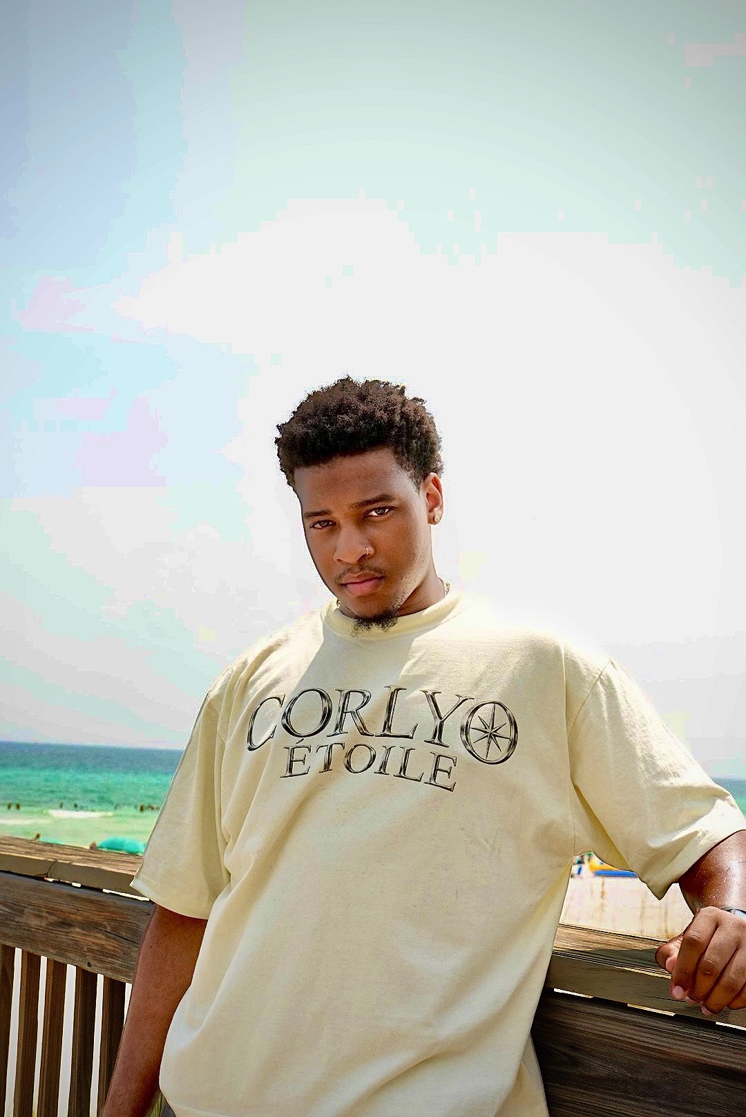 Beachfront portrait in a cream CORLYO Étoile tee against the ocean.