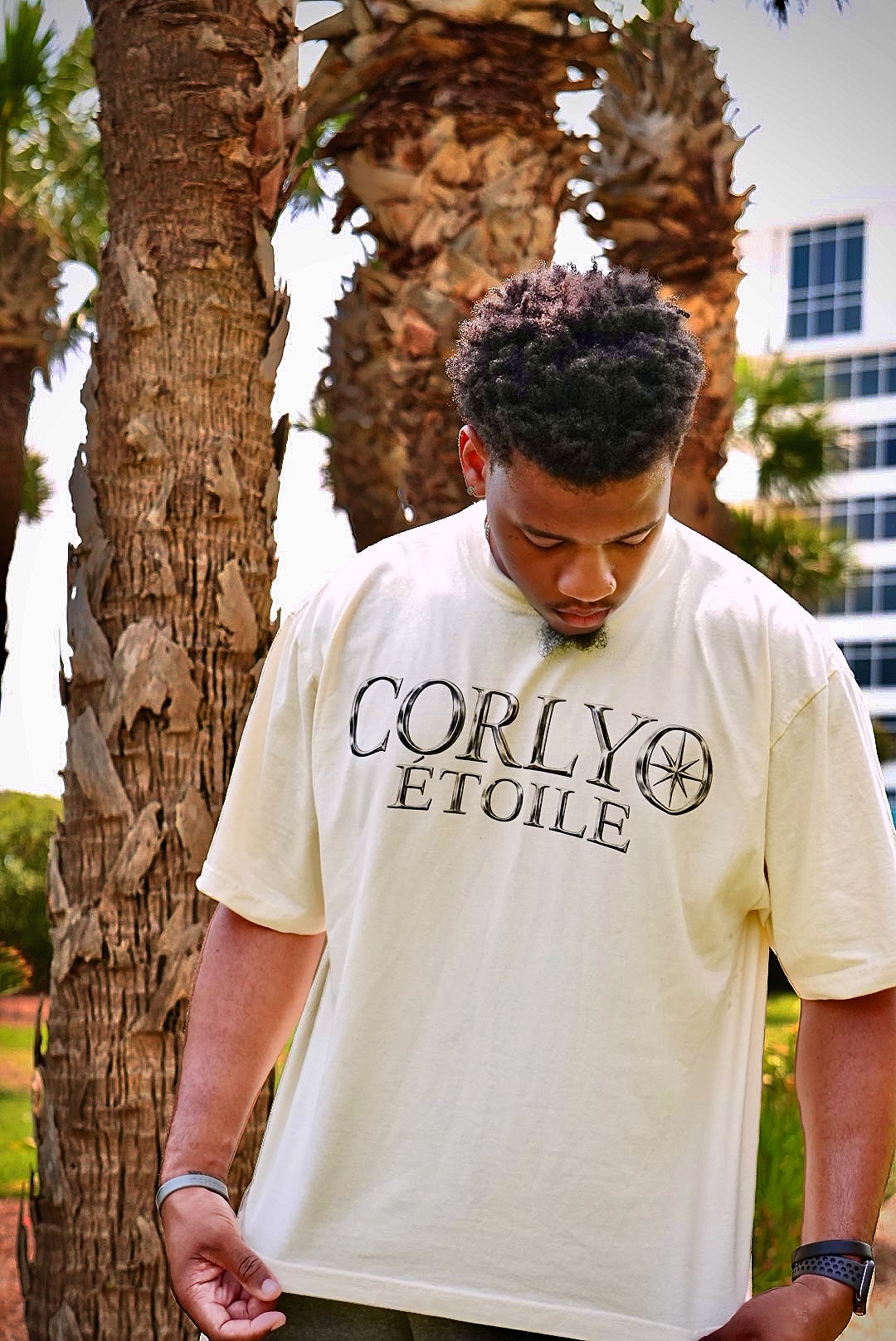 Portrait under palm trees wearing the CORLYO Étoile logo tee.