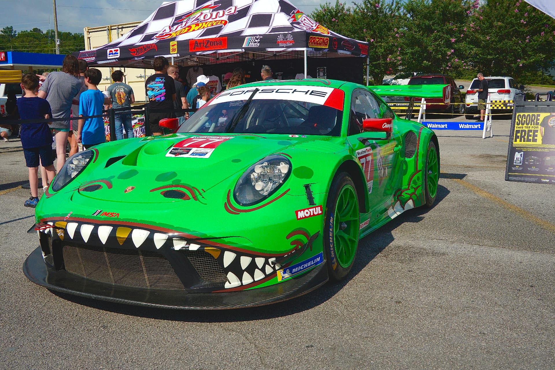 Green Porsche race car with dinosaur livery at a car event.
