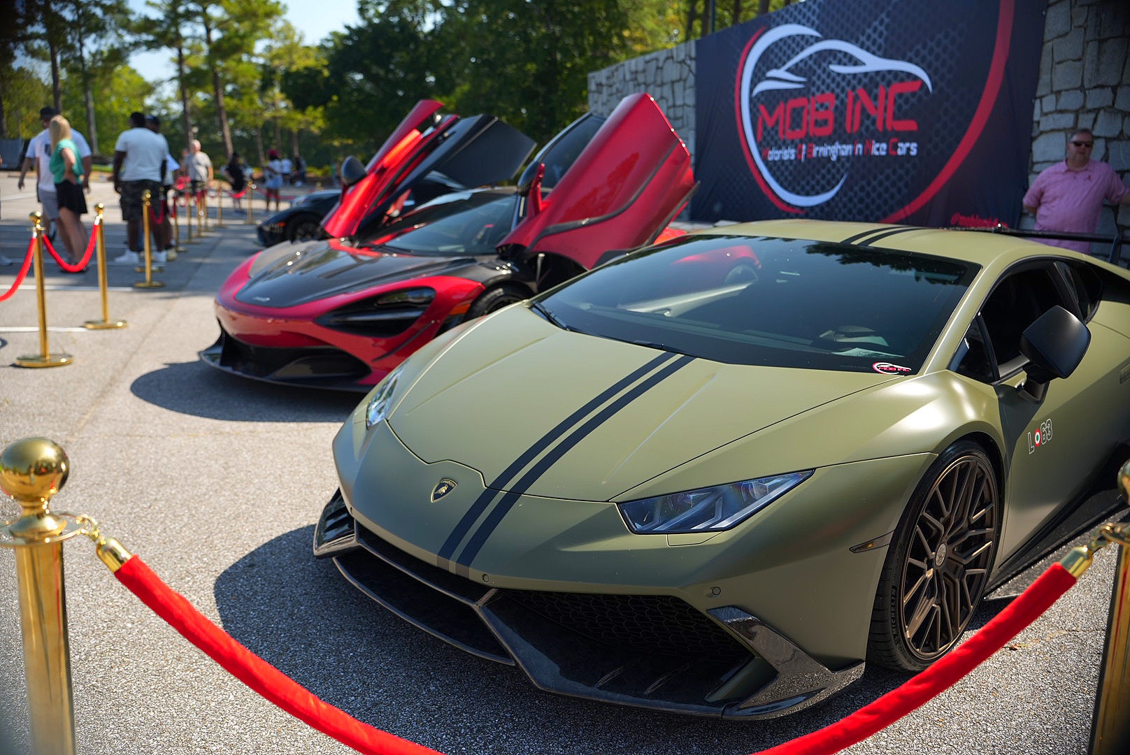 Olive Lamborghini Huracán and red McLaren behind velvet ropes at a car show.