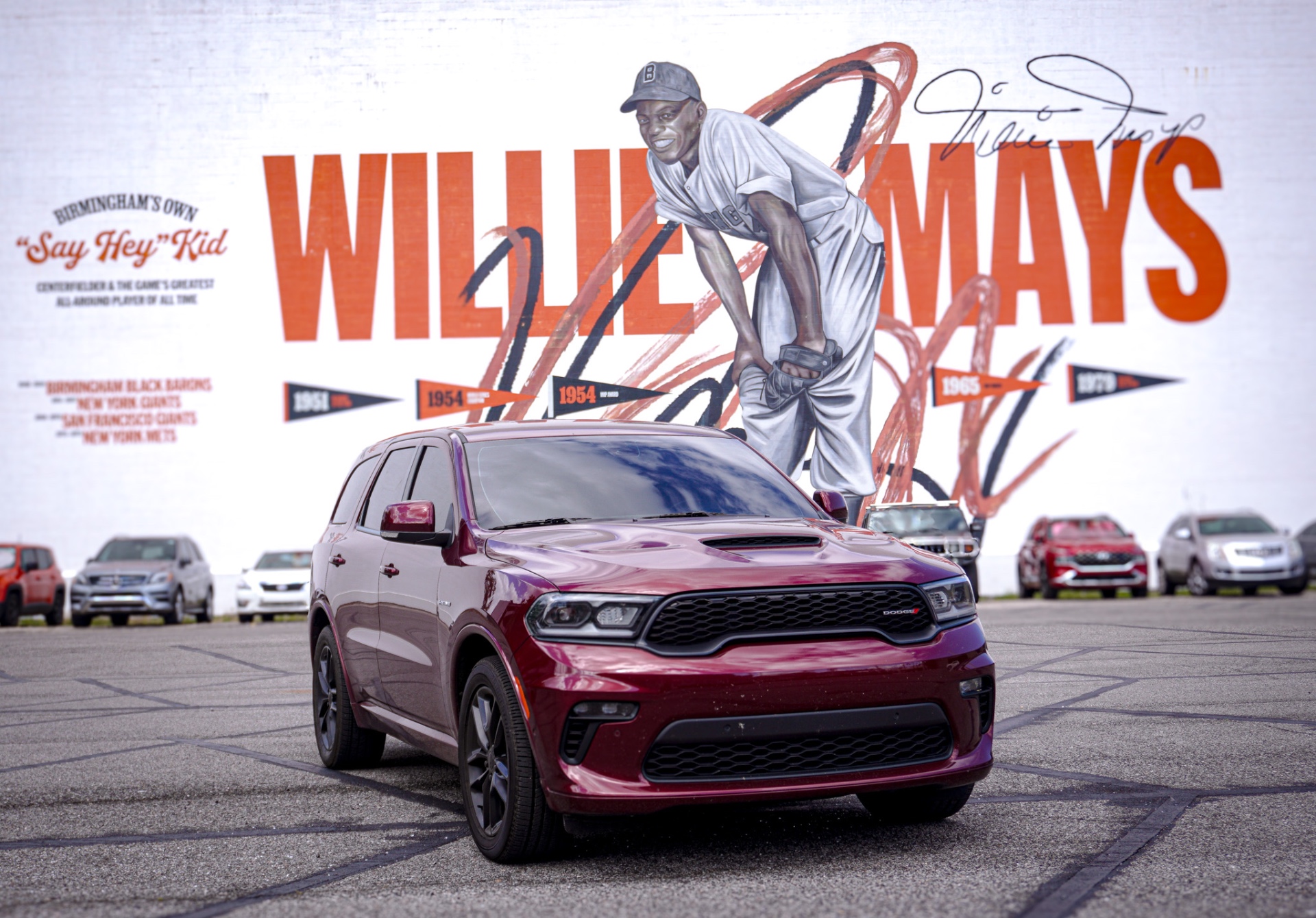Automotive photograph of a maroon SUV in front of a mural.
