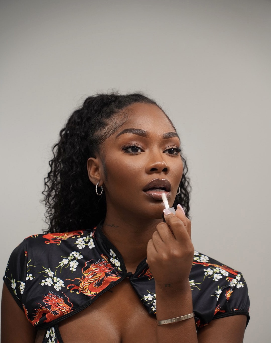Portrait of a woman applying lip gloss in a dragon-print top.