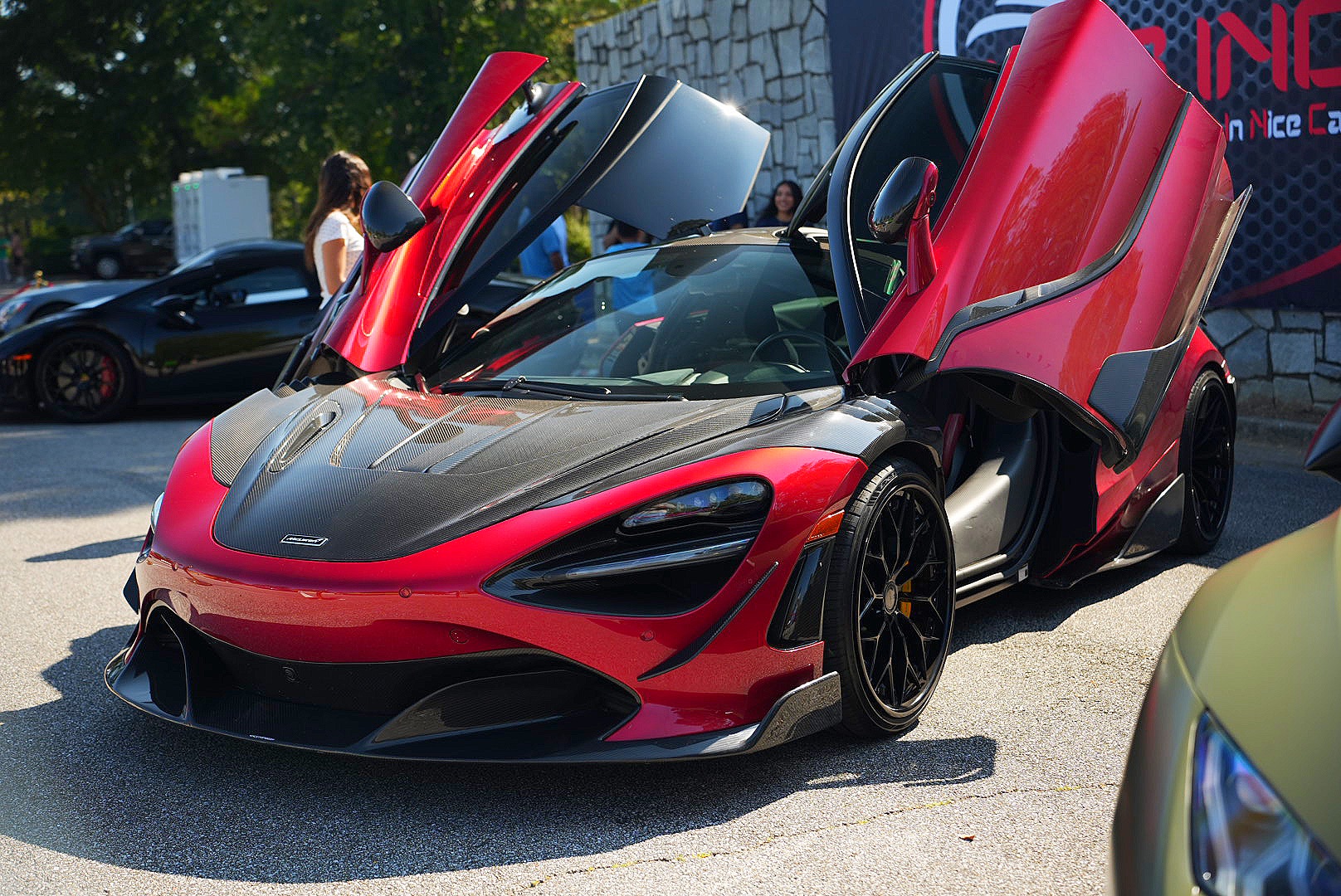 Red McLaren with butterfly doors raised at an exotic car show.